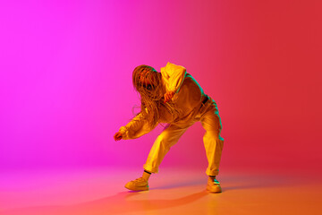 Obraz na płótnie Canvas One young professional hip-hop dancer wearing stylish clothes moving with inspiration over gradient pink background in neon light