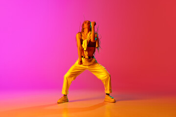 Portrait with one young girl, dancer with dreadlocks dancing over gradient pink background in neon...