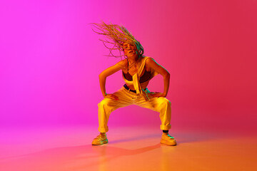 Obraz na płótnie Canvas Portrait with professional dancer with dreadlocks wearing hip-hop stylysh clothes in motion on gradient pink background in neon light. Street style dance