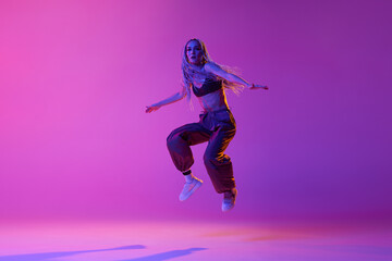 One dancer, woman wearing casual clothes jumping up in motion over gradient purple neon background....