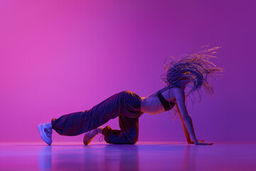 Sexy woman, modern dancer moving in contemporary dance style over purple studio background in neon...