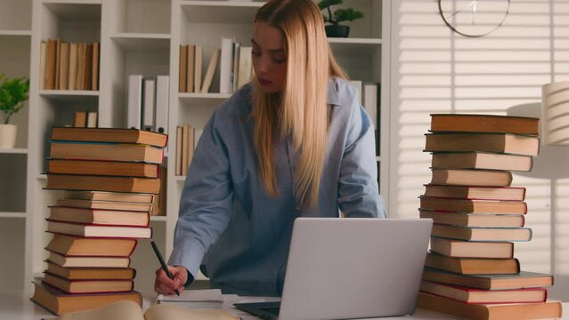 Caucasian student busy girl woman high school pupil studying homework writing task laptop books e-learning online prepare test exam study at library cram SAT test bookworm research history prep course