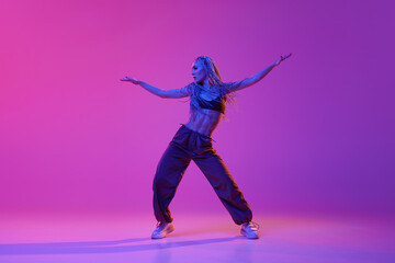 Stylish sporty girl, modern dancer moving to the beat of music over purple studio background in neon light. Freedom
