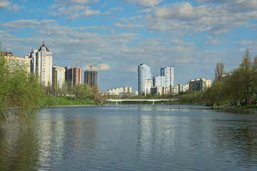Fototapeta na wymiar Wide-angle landscape view of water channel near Rusanivka neighborhood. High water in Kyiv, spring 2023, Ukraine. Residential high-rise buildings in the background against blue sky. Flooding