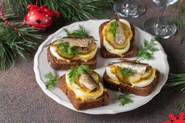 Homemade hot sandwiches with sprats, egg, cheese and pickled cucumber on plate on brown background
