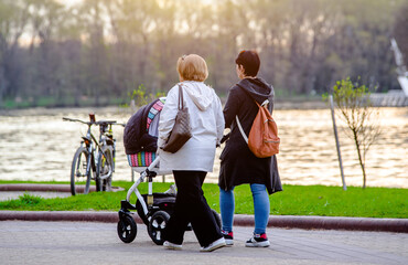 Two girls with a baby stroller are walking in the summer park
