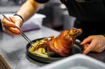chef hand cooking Baked Pork knuckle with vegetables on plate in kitchen