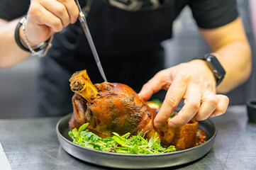 chef hand cooking Baked Pork knuckle with vegetables on plate in kitchen