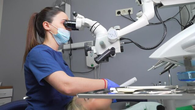 Female dentist using dental microscope treating patient teeth dental clinic office. undergoing treatment by experienced dentist using microscope. Image of woman on patient's chair in dentist's office.