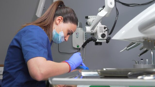 Dentist's hands in gloves with dental punch and cofferdam scarf. Dentist treats woman's tooth to patient with rubber dam. Modern dental office. Treatment elimination of caries, installation of filling