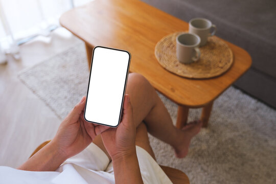 Top view mockup image of a woman holding and using mobile phone with blank desktop white screen at home