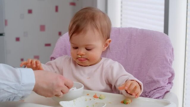 Toddler eat with a spoon, new skill in learning how to eat by himself. Funny baby girl on stage to weaning