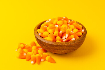 Candy corn. Classic white, orange and yellow Halloween lollipops. Sweet pumpkin gummies in a wooden bowl on a yellow background.Copy space.Place for text. Holiday concept.