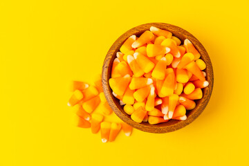 Candy corn. Classic white, orange and yellow Halloween lollipops. Sweet pumpkin gummies in a wooden bowl on a yellow background.Copy space.Place for text. Holiday concept.