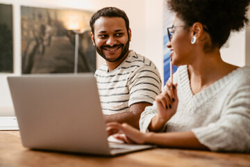Indian man smiling and looking at his wife while she working on laptop sitting at table