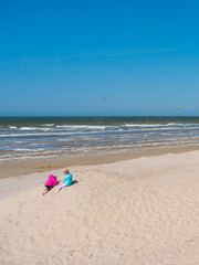 Fototapeta na wymiar Enfant jouant sur le sable et regardant les kitesurfs