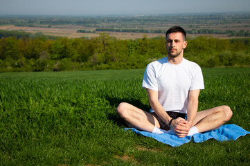 Fototapeta premium a young guy in a white shirt meditates in nature with a beautiful view 