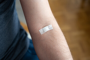 Small plaster or bandaid on the arm of an unrecognizable Caucasian male. Plastered on the elbow pit...