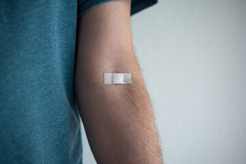 Small plaster or bandaid on the arm of an unrecognizable Caucasian male. Plastered on the elbow pit to stop bleeding after blood collection