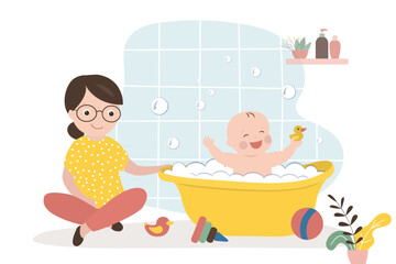 Childhood, caucasian mother helps infant bathes in a baby bath. Funny baby bathes in foam and toys. Hygiene, daily routine for cleanliness and health. Bathroom interior.