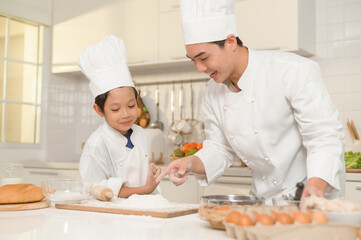 Young Asian father and his son wearing chef uniform baking together in kitchen at home