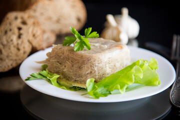 Boiled chicken meat aspic in meat gelatin broth in a plate