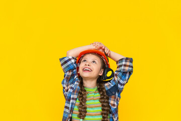A happy young girl in a construction helmet holds a roulette tool. The child is preparing for...