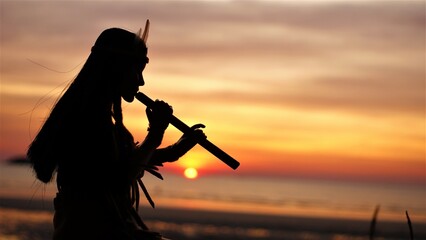 A Native American Indian plays music on a bamboo flute.