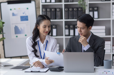 Fototapeta premium Two employees working at table in a modern office, Asian man and a woman work at office desk, Business campaign result and project planning concept, financial planning, 