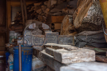 Old vise on a workbench among firewood and sawdust.