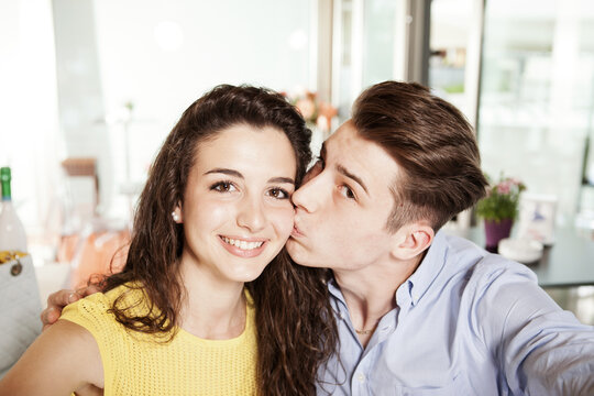 Portrait of a young smiling in love couple taking a selfie. Young smiling boyfriend kiss her smiling girlfriend on her cheek and take a photo together. Young couple in love taking pictures together.