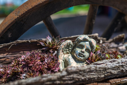 A small angel figure with a wooden wagon wheel and succulents in the background