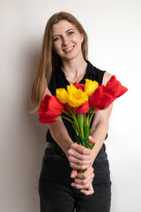 Portrait of young pretty woman, smiling and holding beautiful bouquet of flowers red tulips on white background. Spring, happiness and celebration concept.