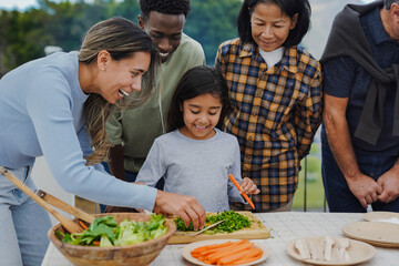 Multi generational people cooking together at home terrace rooftop - Multiracial friends cutting vegetable with  female child outdoor during weekend day