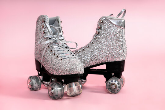 Pair of glitter silver stylish roller skates on pink background.