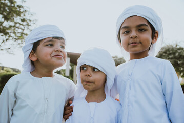 Children playing together in Dubai in the park. Group of kids wearing traditional kandura white dress from arab emirates