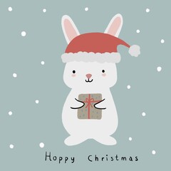 Cute white rabbit wearing Santa Clause hat holding a gift box isolated on pastel green background with snow in hand drawn style. Hand written text Hoppy Christmas. Greeting card design.