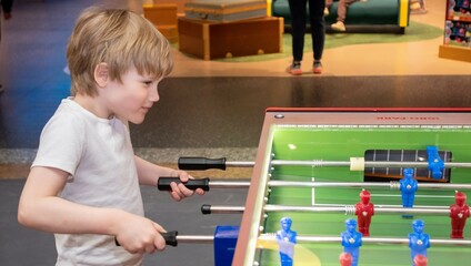 A boy is playing table football. Game. White hair Blond, European appearance, blue eyes.