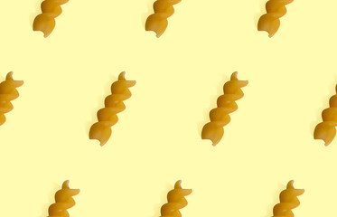 Uncooked fusilli pasta isolated on yellow seamless background. Itallian spiral pasta close-up on orange seamless pattern
