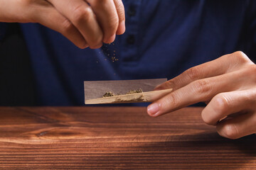The hands of a person assembling a joint, carrying cannabis flowers from above.