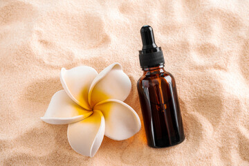 Top view essential oil and plumeria flower on a sandy beach.