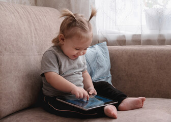 Happy little child sitting on sofa and using tablet.
