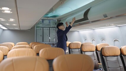 Asian man flight attendant closing the overhead luggage compartment lid for carry on baggage...