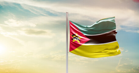 Mozambique national flag waving in beautiful sky. The symbol of the state on wavy silk fabric. - obrazy, fototapety, plakaty