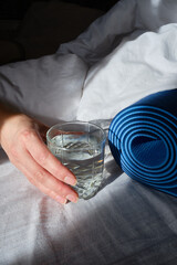 A yoga mat and a glass of water in the hands of a girl close-up on a light background. Health and sport concept