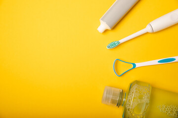 Sonic electric toothbrush, toothpaste, mouthwash, dental floss and tongue cleaner on yellow...
