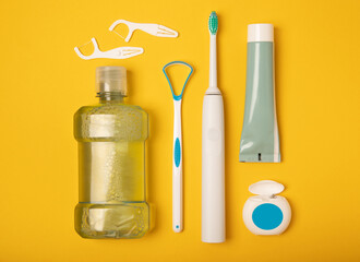 Sonic electric toothbrush, toothpaste, mouthwash, dental floss and tongue cleaner on yellow...