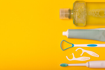 Sonic electric toothbrush, toothpaste, mouthwash, dental floss and tongue cleaner on yellow...