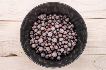 Frozen black currant with black plate on wooden table, macro, top view.