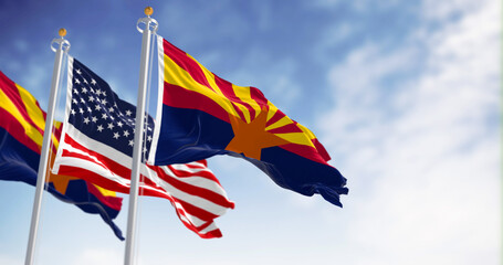 The flags of Arizona and United States waving in the wind on a clear day